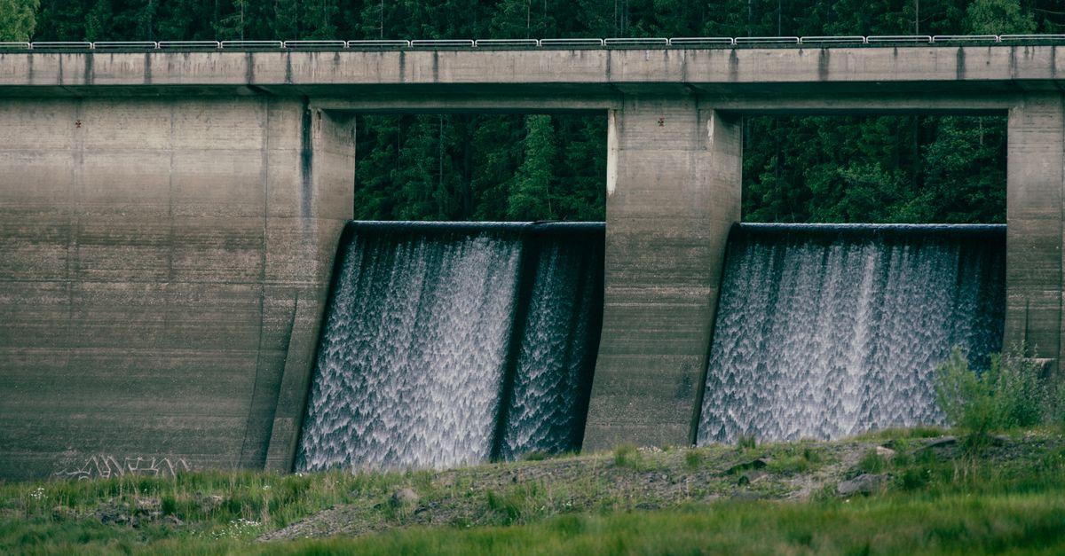 Concrete dam with flowing water surrounded by lush greenery, showcasing nature and engineering.